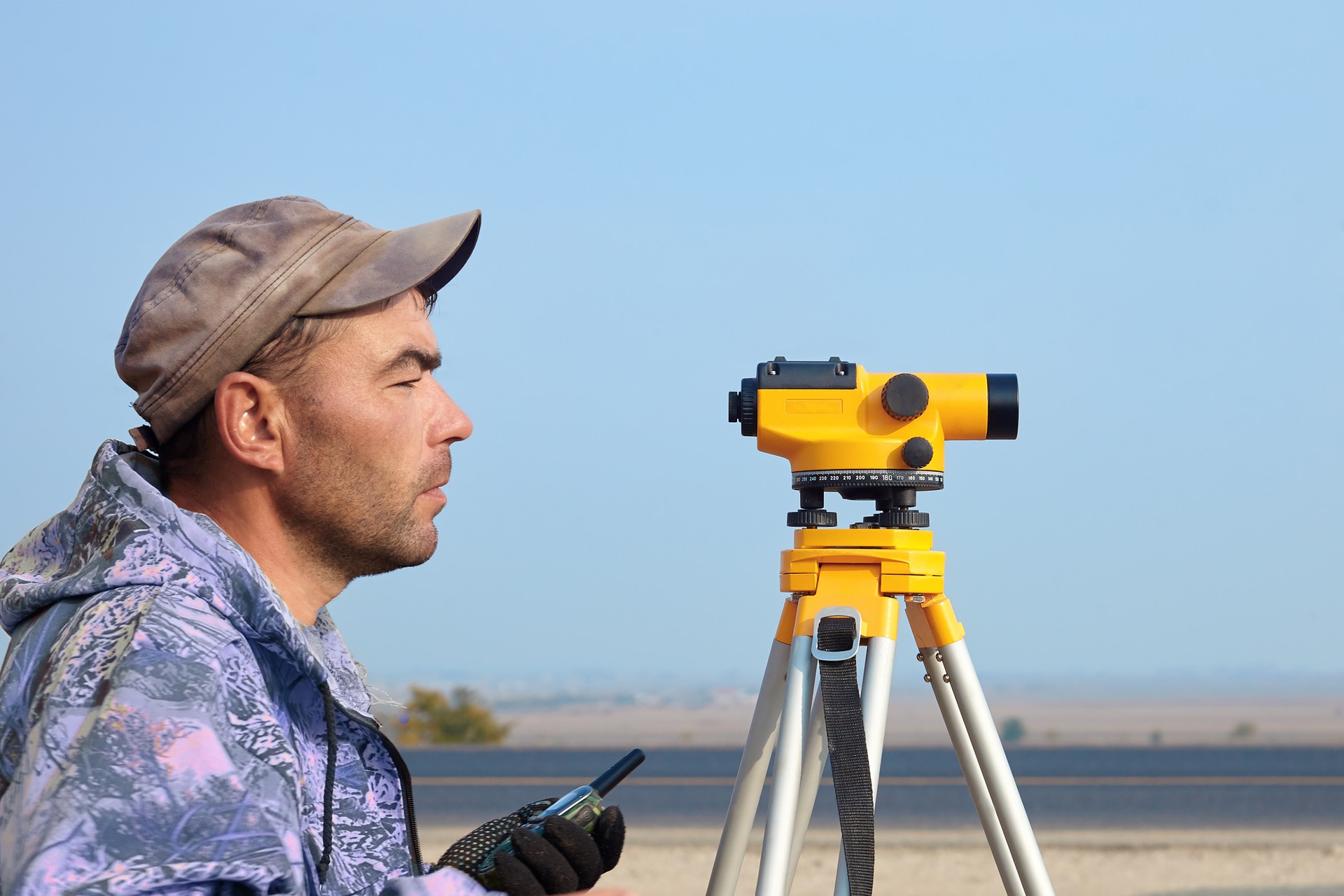 Worker with level, surveyor builder with geodesy equipment close to highway, with mobile phone.